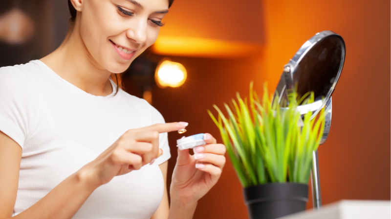Women putting contact lens in container with plant in the background